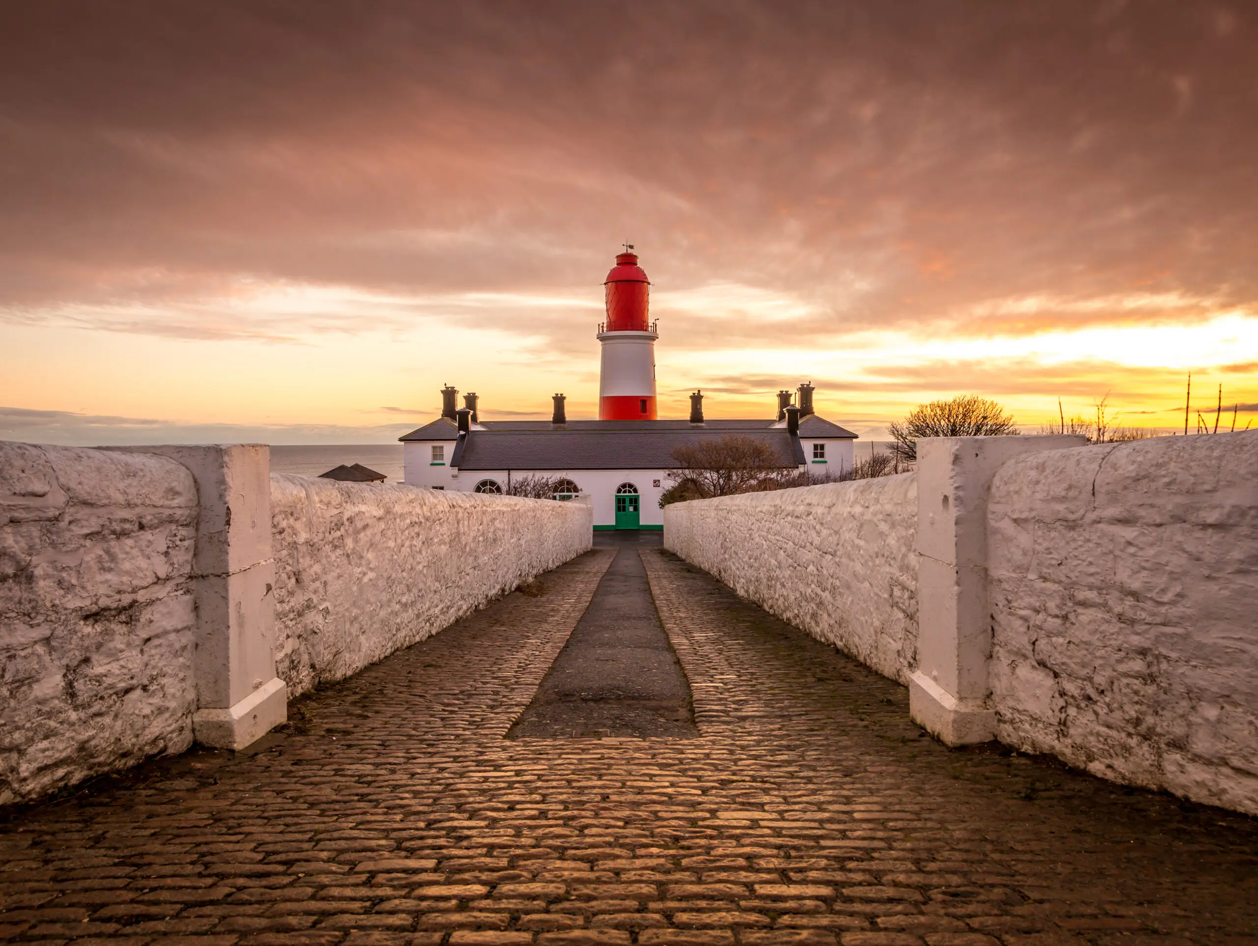 Image of a lighthouse behind a small white building in Tyneside where we do Pat Testing