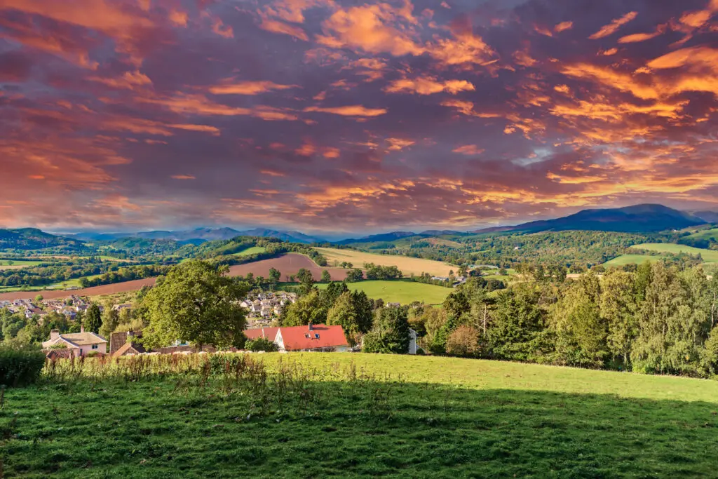 The Scottish hillside looking over some residential housing onto the fields hillside and distant mountains that watch over the highland village of Crieff in Scotland.